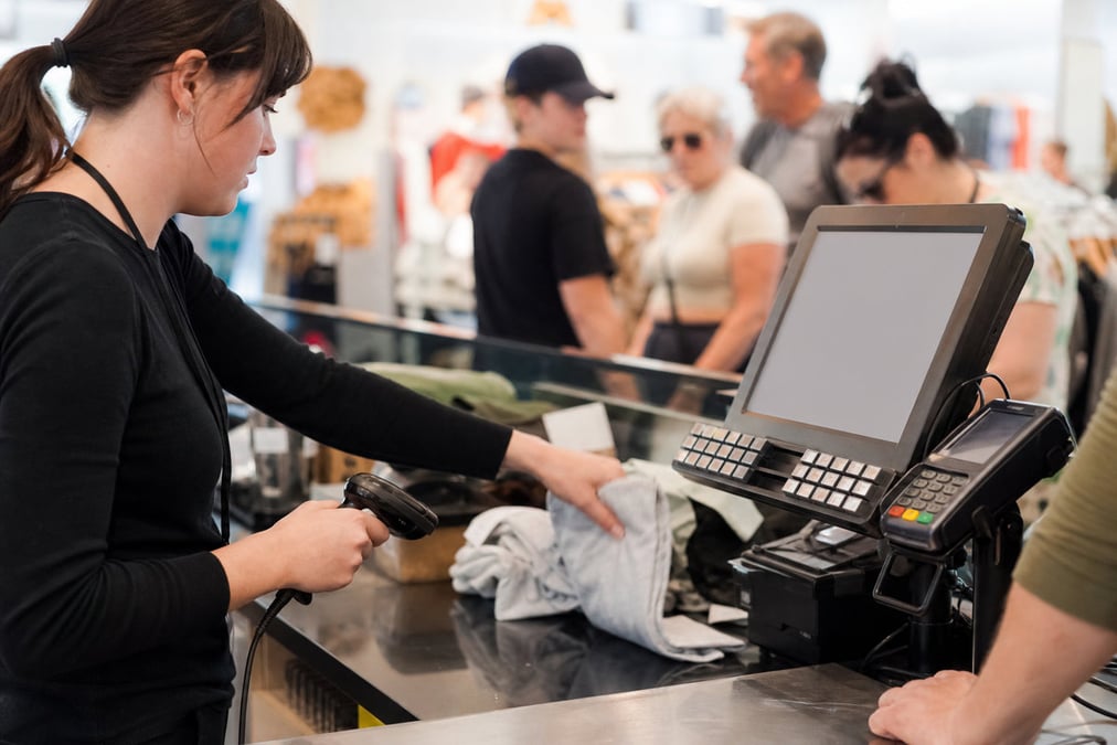 Cashier handing a takeaway bag to a customer with a contactless payment terminal in focus.