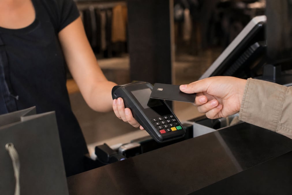 A person using a payment terminal with a laptop and a notebook on a work desk, illustrating cashless transactions.