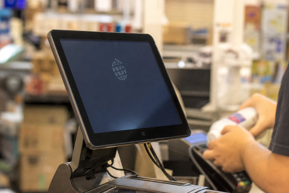 A restaurant employee uses a touchscreen register in a modern cafe setting with natural light.