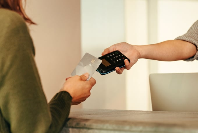Customer handing a card to a smiling staff member holding an EFTPOS terminal at a shop counter