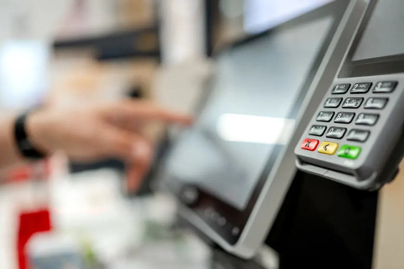 Close-up of a checkout terminal keypad with a hand tapping the POS screen behind it